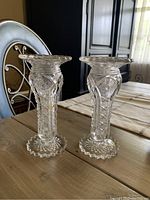 Photo of two clear cut glass vases placed on wooden table, showing detailed intricate cut patterns and scalloped edges at base and top rim.