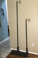 Two adjustable metal clothing display racks standing side by side against a wall, showing full height and base details.