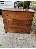 Front view of antique wooden secretary desk showing four drawers with brass pull handles and wood surface with scratches.