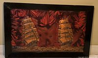 Framed copper embossed wall art featuring two sailing ships with textured red and brown background