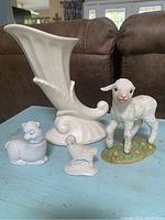 Photo of ceramic cornucopia vase and three lamb figurines together on a blue surface.