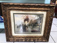 Ornate framed print of ladies on a street with trees, lamps, and buildings in muted colors