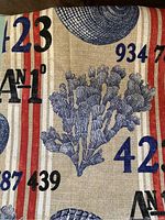 Photo shows nautical fabric with blue coral, shells, and numbers in blue and black with red and white vertical stripes on beige background.
