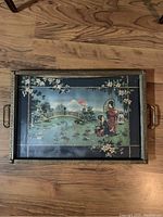 Top view of rectangular vintage serving tray with oriental design under glass, metal frame and handles, placed on wood floor.