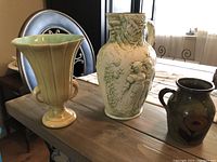Three vintage ceramic items on wooden table: two pitchers and one flower vase displaying unique vintage designs and colors.