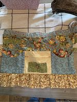 Front view of handmade shabby chic apron showing patchwork fabric design, pocket with button, and ruffled bottom trim.