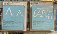 Two Martha Stewart stencil sets showing monogram serif uppercase and lowercase letters and Italian flourish decorative script letters, each in original plastic packaging.