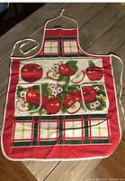 Photo of vintage Unitex apron laid flat showing red apples and plaid pattern.