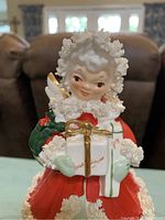 Front view of Napco Christmas angel figurine in red and white dress holding wrapped gifts