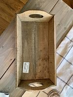 Top-down photo of a rectangular wooden tray with two oval cutout handles on each short end, visible natural wood grain and light wear.
