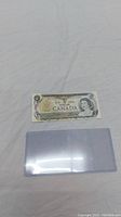 Front and part of back of the 1973 Canadian one dollar bill along with a protective plastic sleeve below it.