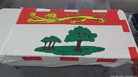 Flag of Prince Edward Island spread out showing the full design including the lion and trees on a white background with red border.