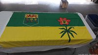 Full view of the Saskatchewan flag laid out flat, showing green and yellow bands with shield emblem and red lily flower.