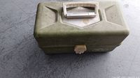 Closed vintage olive-green plastic tackle box with white handle and latch on a floor surface.