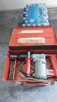 Hilti TE-17 hammer drill inside red metal carrying case with some drill bits visible and a case lid open, showing contents