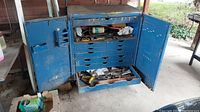 Photo of large blue metal rolling tool box with open doors showing multiple drawers and a bottom tray with tools inside.