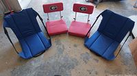 Photo of two red folding stadium seats with 'G' logos and two blue padded folding seats arranged on the floor.
