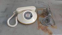 Full view of vintage 1980s cream/beige pancake rotary phone showing handset, base with rotary dial, coiled handset cord and base cord.