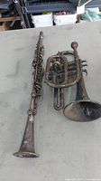 Vintage Coronet cornet and incomplete clarinet placed side by side on table showing tarnished and damaged conditions