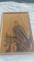 Full view of the wood panel carving showing the eagle perched on a tree branch with background trees and wooden frame.