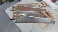 Four vintage hand saws arranged on a table showing different sizes and handle designs, some blades showing rust and wear.