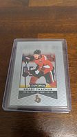 Single photo showing a Brady Tkachuk rookie hockey card in protective sleeve on a wooden surface.