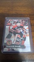 Photo of the Dominik Hasek rookie hockey card in black and orange goalie kit in a protective plastic sleeve.