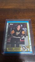 Photo of a Topps hockey card featuring Mario Lemieux in Pittsburgh Penguins uniform enclosed in a protective plastic sleeve.