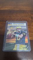 Photo of 1999 Tom Brady Michigan football trading card in plastic sleeve on wooden surface.