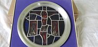 Front view of round stained glass plate with religious crucifixion motif in silver frame on purple backing.