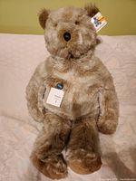 Photo of a large grey Gund teddy bear plush sitting upright, showing the detailed face, nose, and fur texture with attached brand and product tags.
