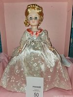 Front view of Madame Alexander First Lady Doll wearing cream floral satin gown with peach collar, displayed standing inside a pink box.
