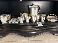 Wide view the full tea set arranged on a carved wooden display base showing cups, teapot, sugar bowl, cream pitcher, candy dish, and salt cellars with spoons.