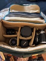 Top-down view of padded camera gear bag showing camera body and three lenses in compartments.