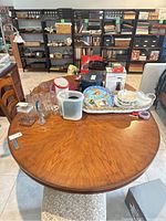 Top-down view of the round wood dining table with various household items on it and shelving in background.