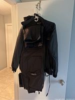 Full view of black motorcycle gear suit with zipper and multiple pockets, hung on a hook.