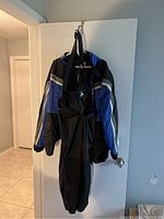 Full view of the blue and black Tour Master motorcycle rain suit jacket hanging along with black bib rain pants on a door.