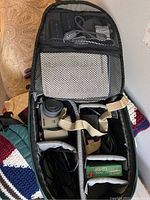 Open Canon backpack showing organized compartments containing Sony digital camera, cables, and CDs.