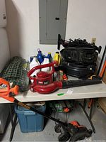 Overview photo showing Toro red leaf blower, Black & Decker string trimmer, green garden fencing roll, and assorted bottles of automotive and lawn care liquids on a table.