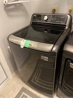 Front three-quarter view of LG top-load washing machine in dark graphite with glass lid closed.