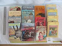 Top view showing 15 classic children's books arranged in rows with visible titles and covers, alongside a ruler for size reference.