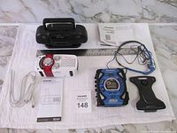 Top-down view of all three items with accessories and paperwork on white cloth surface with ruler for scale.