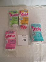 Top-down view of four unopened McDonald's Barbie collectables in pink, green, orange, and blue packaging displayed on a white surface.
