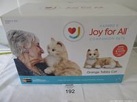 Box featuring Joy For All Companion Pet branding, photo of an older woman interacting with the orange tabby cat toy, age recommendation 5-105.