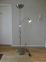 Full view of the brushed chrome floor lamp showing the main uplight, adjustable extendable sliding arm with smaller reading spotlight, and base with power cord and footswitch.