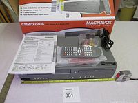 Overall lot photo showing the combo unit, remote, paperwork, and original box on table with measuring tape nearby.