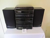 Full view of the black Memorex Midi HiFi system including two speakers placed on either side, all components stacked vertically, unit on white table against wall.