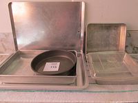 Image showing various baking pans including a rectangular aluminum pan, round pan, and cookie sheets stacked on a countertop.