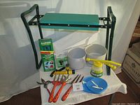 Full display of gardening bench, planters, pots, sprayer, tools, and accessories on a white cloth.