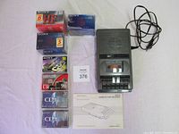 Top view of Realistic cassette player with power cord, instruction manual, and seven unopened cassette tape packages of various brands and durations arranged next to it.
